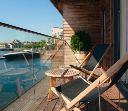 Balkong med två solstolar och ett litet bord på Slottsholmens flytande hotellrum, med utsikt över vattnet.