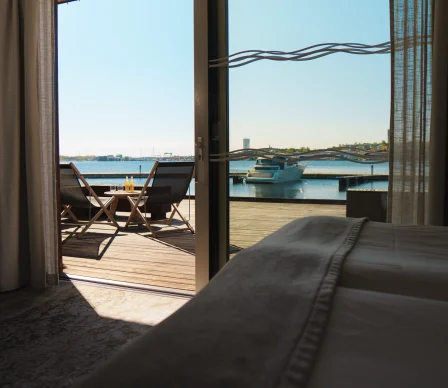 Hotellrum med terrass med utsikt över vatten och en brygga med båtar på Slottsholmens flytande hotell.