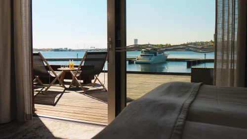 Hotellrum med terrass med utsikt över vatten och en brygga med båtar på Slottsholmens flytande hotell.