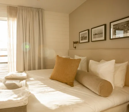 Ljust och stilrent hotellrum med dubbelsäng, mjuka kuddar, ljusa gardiner och inredning i skandinavisk design med varma toner.