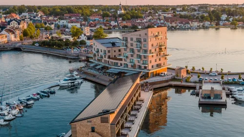 Slottsholmen hotell i rosa kvällsljus med spegelblankt vatten runtom och Västervik i bakgrunden.