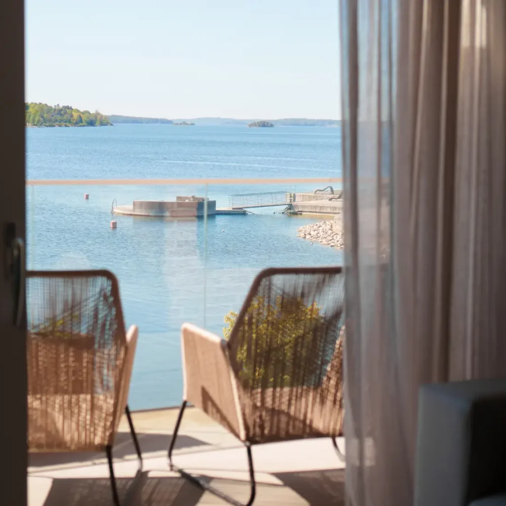 Utsikt över havet och en brygga från hotellrum mot balkong med två stolar.