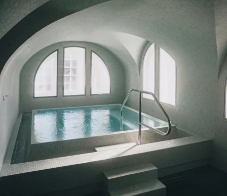 Hamam i mosaik med varmvattenpool, stora välvda fönster och mjukt dagsljus som skapar en rofylld och avslappnande atmosfär.