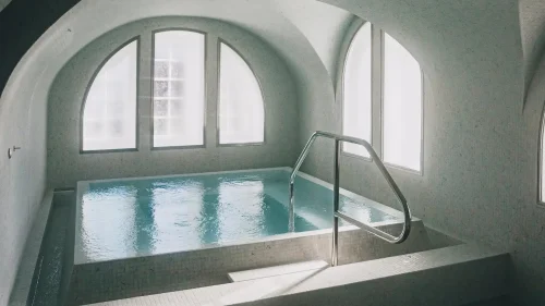 Hamam i mosaik med varmvattenpool, stora välvda fönster och mjukt dagsljus som skapar en rofylld och avslappnande atmosfär.