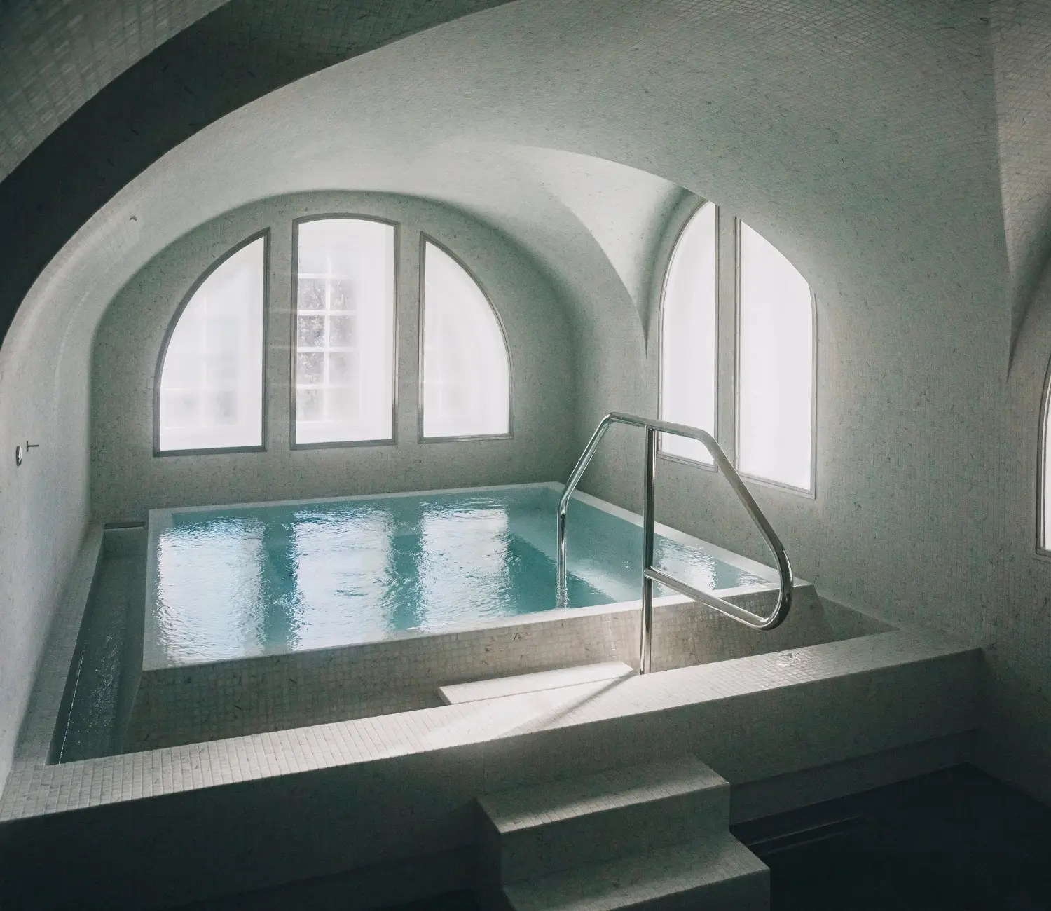 Hamam i mosaik med varmvattenpool, stora välvda fönster och mjukt dagsljus som skapar en rofylld och avslappnande atmosfär.