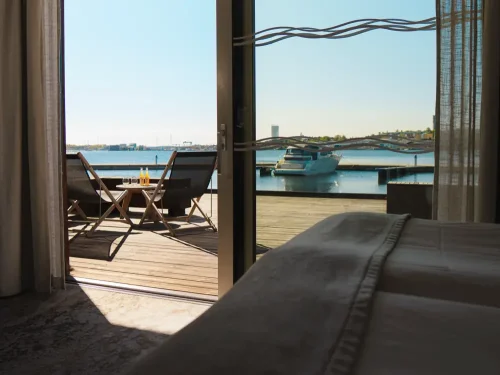 Hotellrum med terrass med utsikt över vatten och en brygga med båtar på Slottsholmens flytande hotell.